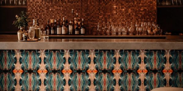 A stylish bar with colorful tile design and various bottles on the counter.