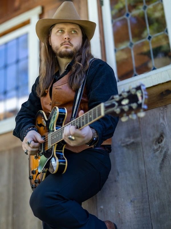 Man in cowboy hat playing electric guitar outdoors.