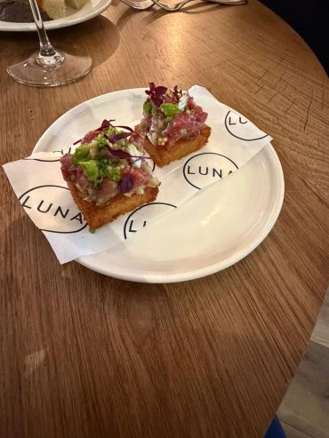 Two gourmet appetizer bites on a white plate with branded paper.