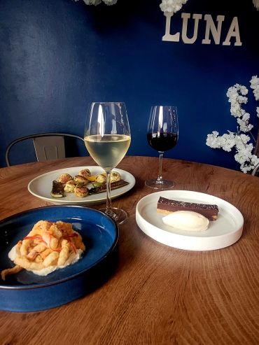 Table with food dishes and wine glasses against a blue wall.