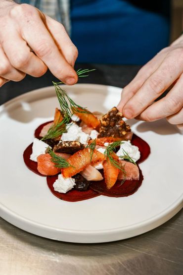 Hands garnish an artfully plated gourmet dish with fresh herbs.