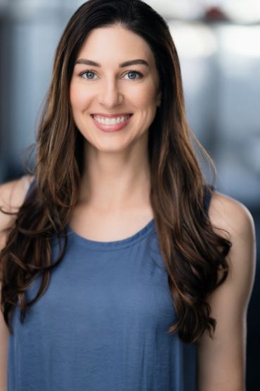 Smiling woman with long brown hair wearing a blue sleeveless top.