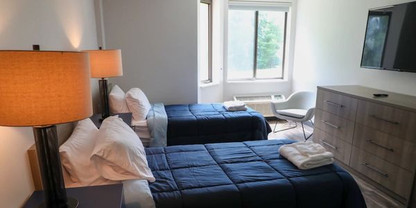 A bright hotel room with two single beds and modern furnishings.