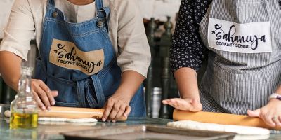 Two people wearing aprons rolling dough in a cooking class.