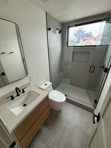Modern bathroom with a glass shower, wooden vanity, and black fixtures.