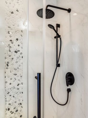 Modern shower with black fixtures and pebble tile accent wall.