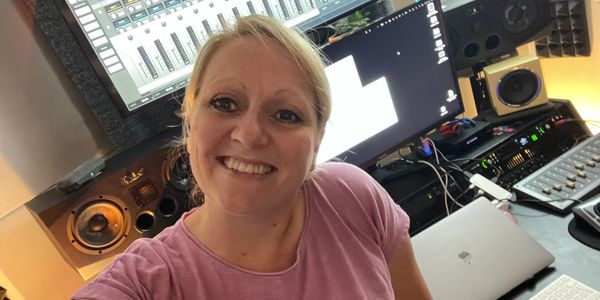 Smiling woman taking a selfie in a music studio with audio equipment.