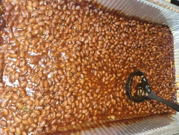A large tray of cooked baked beans with a serving spoon.