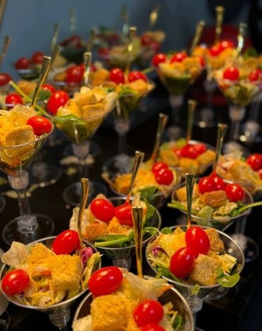 Elegant salad servings in cocktail glasses with cherry tomatoes and golden utensils.