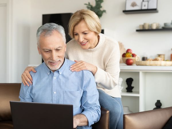 Wife sitting on the couch and holding husband shoulder form the back 