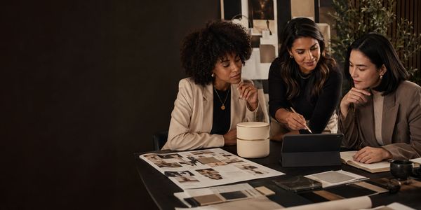Three women collaborating around a tablet and design materials.