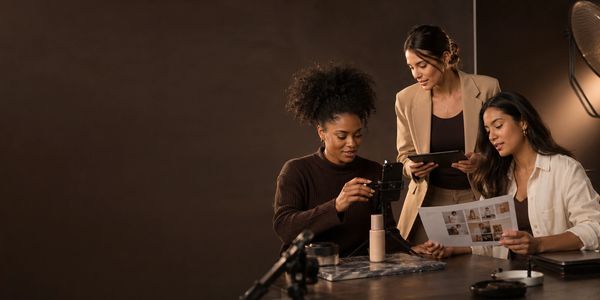 Three women collaborating on content creation using devices and printed photos.