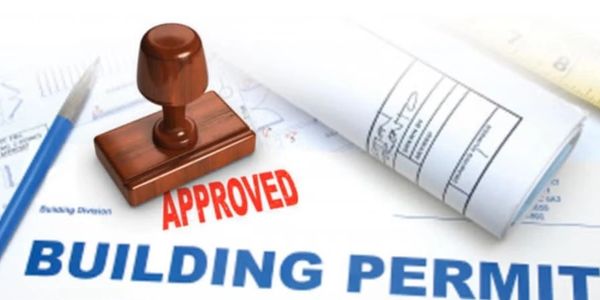 A building permit document stamped with 'APPROVED' and a rolled blueprint.