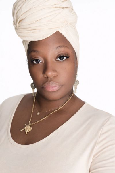 Portrait of a woman wearing a cream headwrap and gold jewelry.