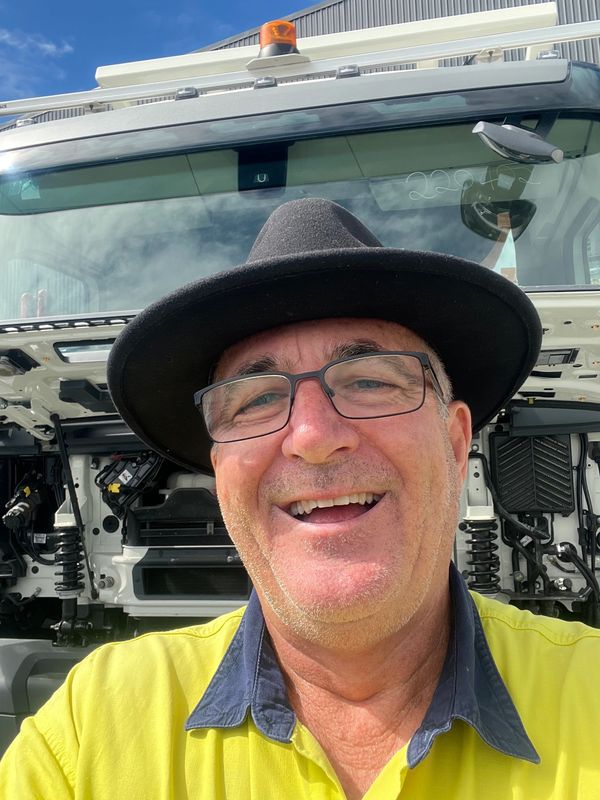 Man wearing glasses and a black hat taking a selfie in front of a vehicle.