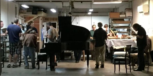People gathered around a grand piano in a dimly lit room.