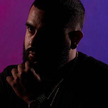 Man with beard in contemplative pose against purple and blue background.