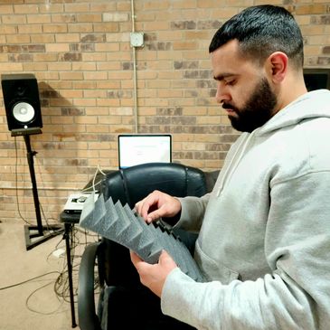 Man in gray hoodie examining soundproof foam in a studio room.