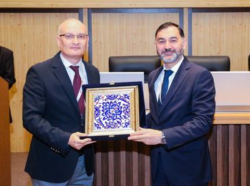 Two men in suits holding a framed decorative tile together.