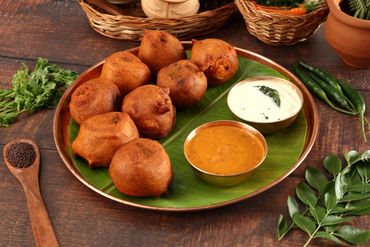Plate of crispy medu vada with chutneys on a banana leaf.