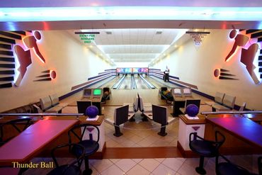 Interior view of a retro bowling alley with vibrant lighting and lanes.