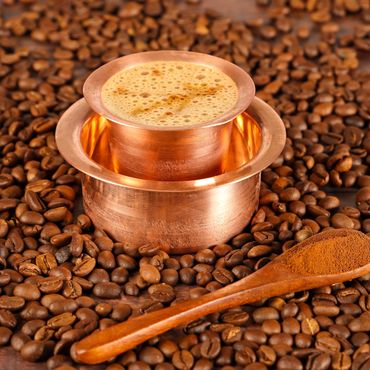 Traditional South Indian coffee served in a copper tumbler and davara with coffee beans and powder.