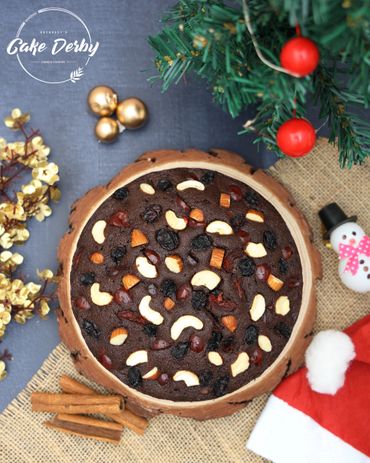 A festive fruitcake decorated with nuts and dried fruits next to Christmas decorations.