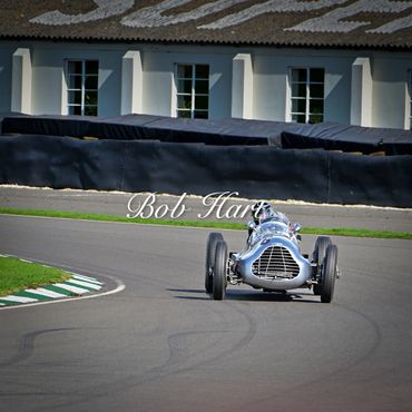 Vintage race car on a curved track near a building.