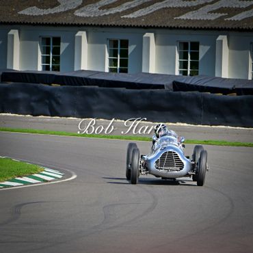 Vintage race car on a curved track near a building.