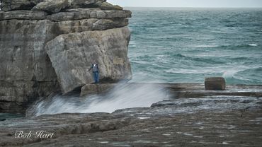 A person fishing on rocky cliffs by the ocean under a cloudy sky.