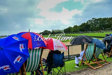 People sitting under branded umbrellas by a riverside on a cloudy day.