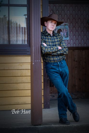 Man in cowboy attire leaning on a post.