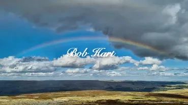 A rainbow arches over a vast landscape with cloudy skies.