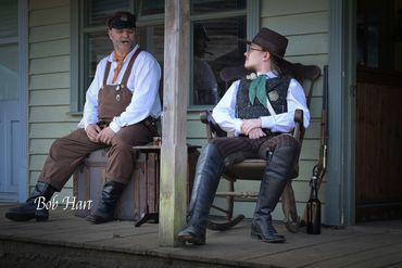 Two men in vintage western attire sitting on a porch.