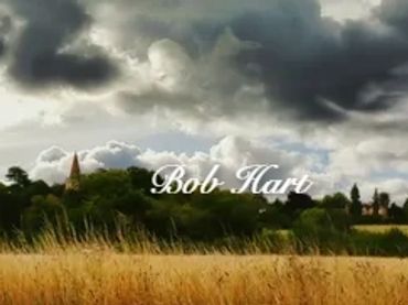 Stormy clouds gather over a golden wheat field with distant trees and buildings.
