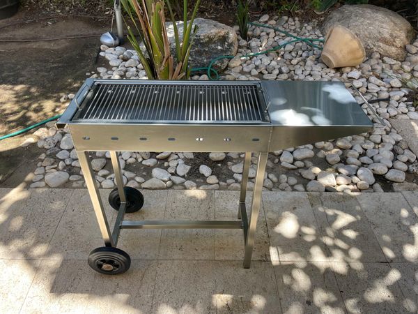 Stainless steel charcoal grill with wheels outdoors.