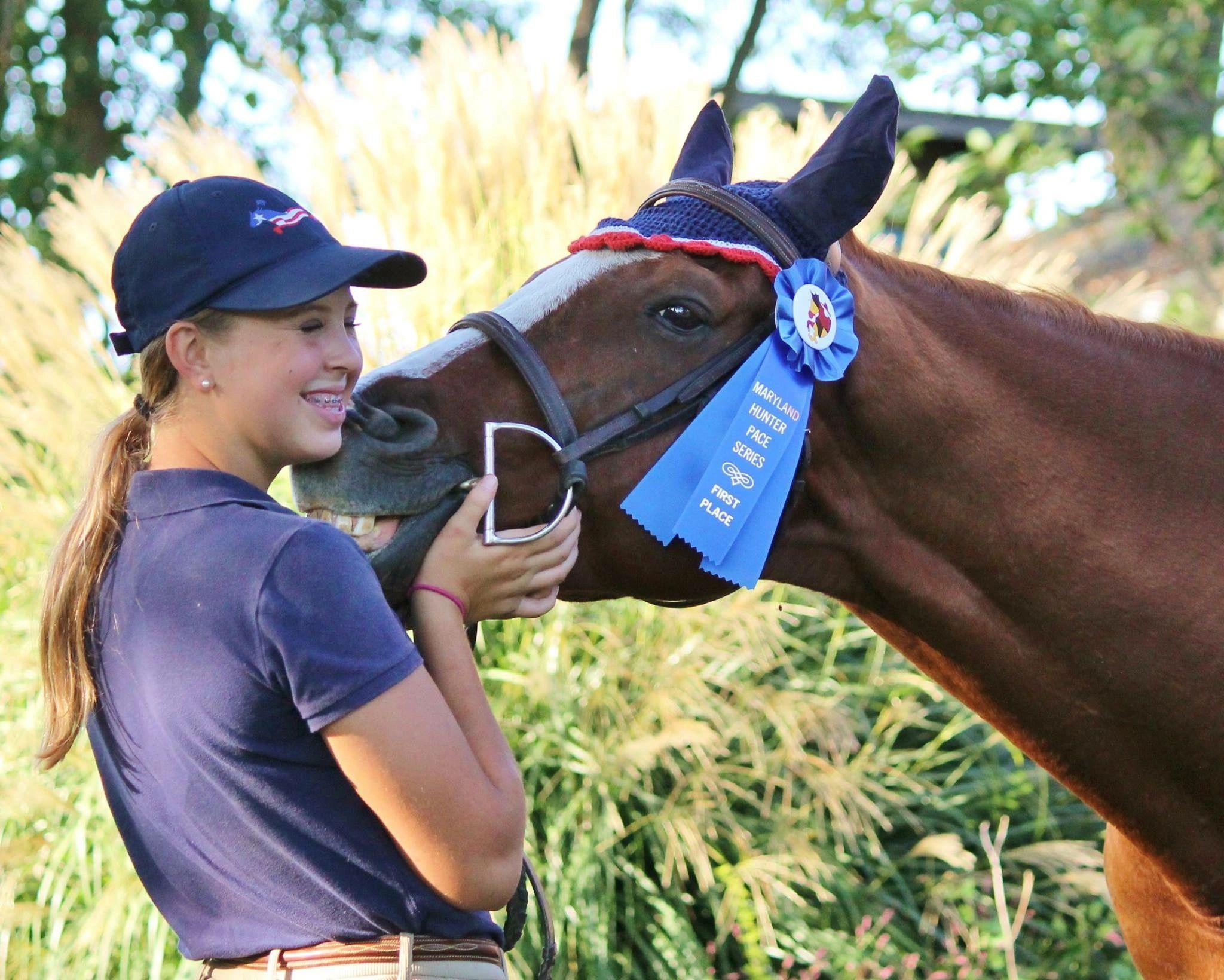 Smiling girl with a horse wearing a first place blue ribbon.