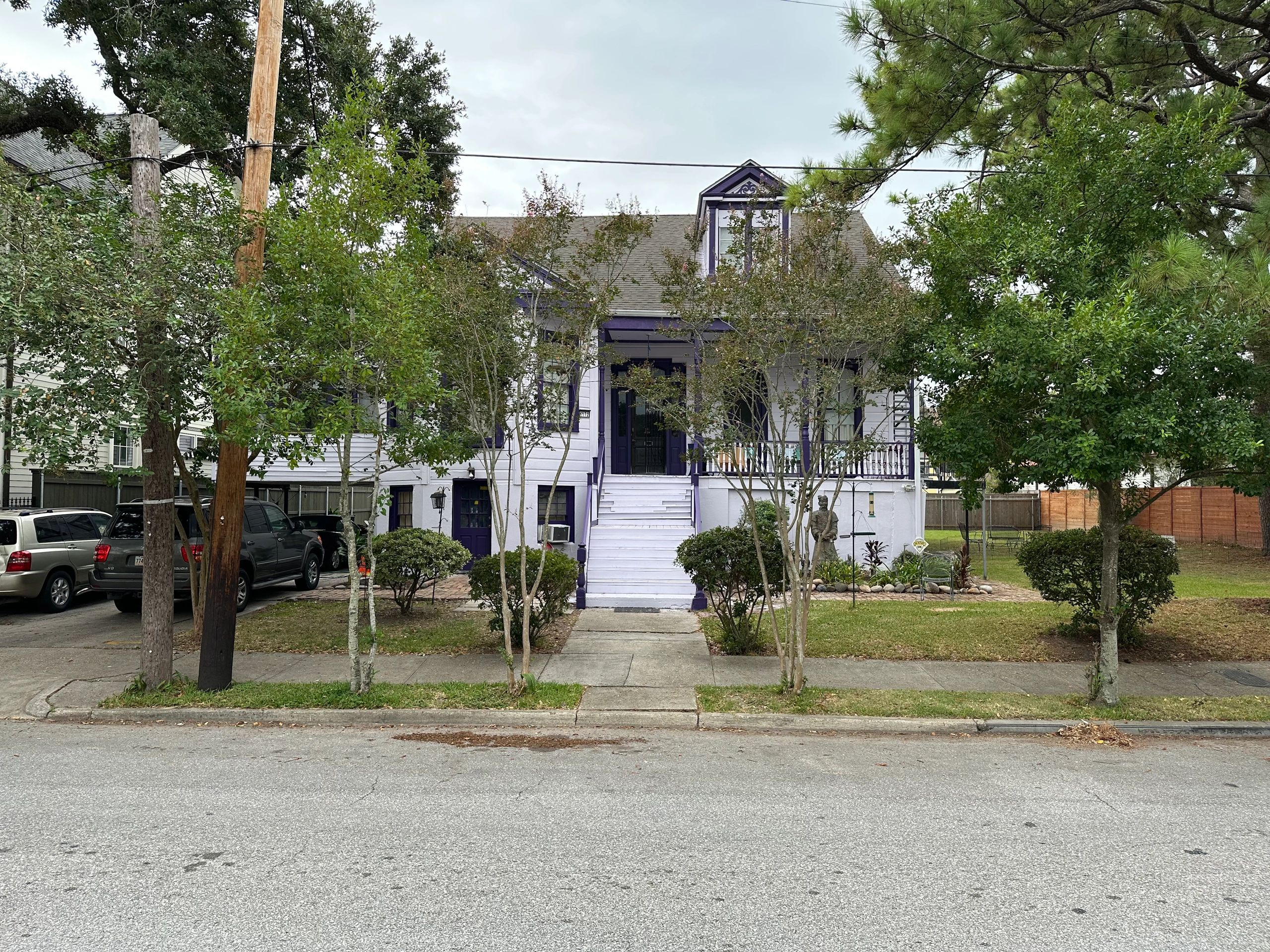 A two-story white house with purple trim and a gray roof, surrounded by trees and a small yard.