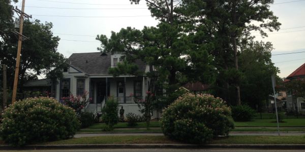 A white house with a gray roof and a large tree in the front yard.