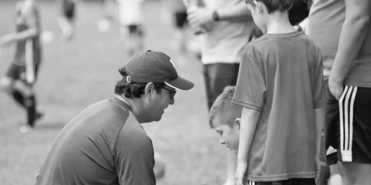 Coach kneels to talk to young soccer players during a game.