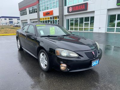 Black Pontiac sedan parked outside a dealership on a rainy day.
