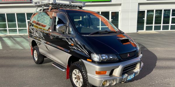 Black and silver off-road van with roof rack parked outside a building.