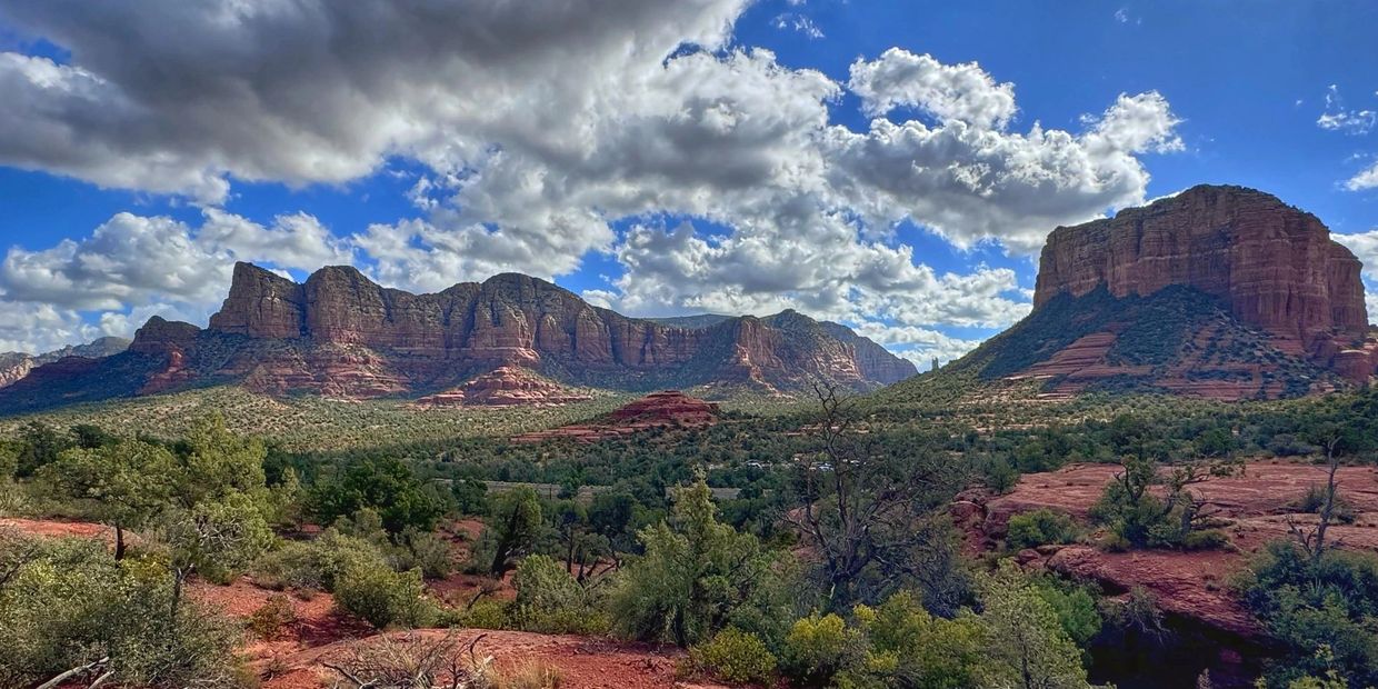 Red rock formations and green vegetation under a partly cloudy blue sky.