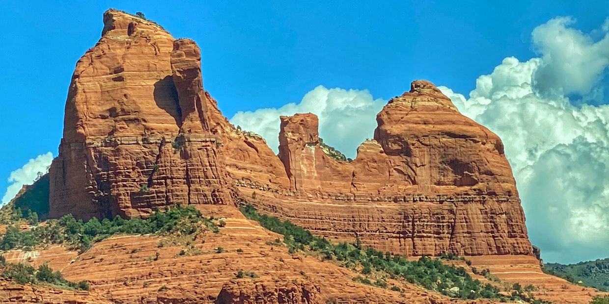 Majestic red rock formations under a bright blue sky with fluffy clouds.