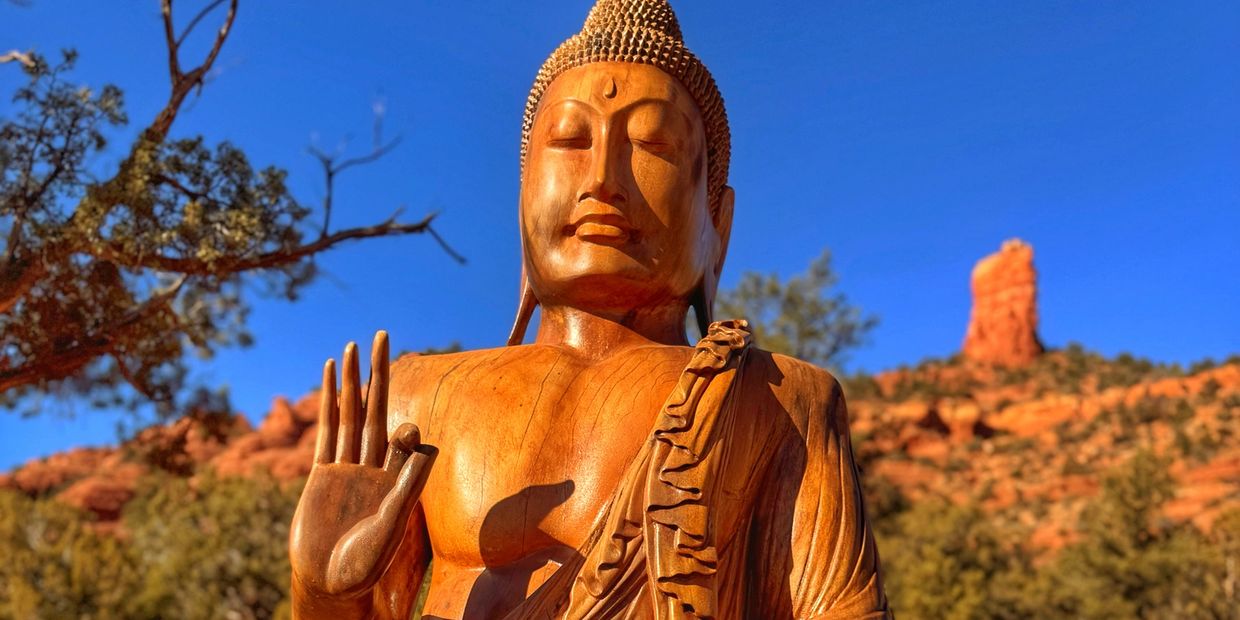 Wooden Buddha statue with serene expression against a desert landscape.