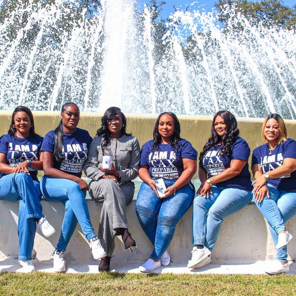 Group of women posing in front of a fountain, most wearing matching tax preparer shirts.