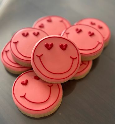 Pink smiley face cookies with heart-shaped eyes arranged on a surface.