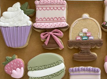 Colorful decorated cookies shaped like cupcakes, strawberries, cakes, and macarons.