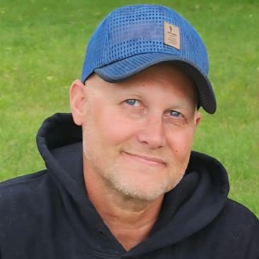 Man wearing blue cap and black hoodie outdoors.