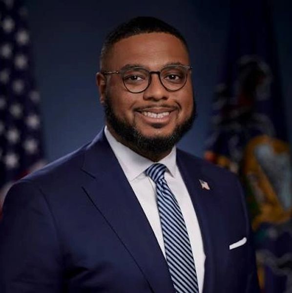 Man in suit with glasses smiling in formal portrait.